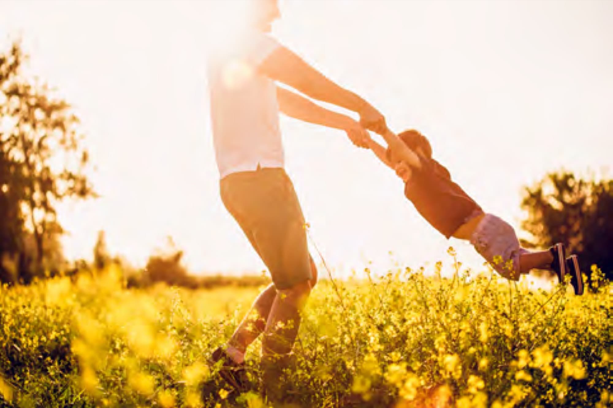 Father swinging his child through a sunlit meadow in Arabian Ranches 3. AR3 Living is your go-to on-the-ground expert for buying property in the community.