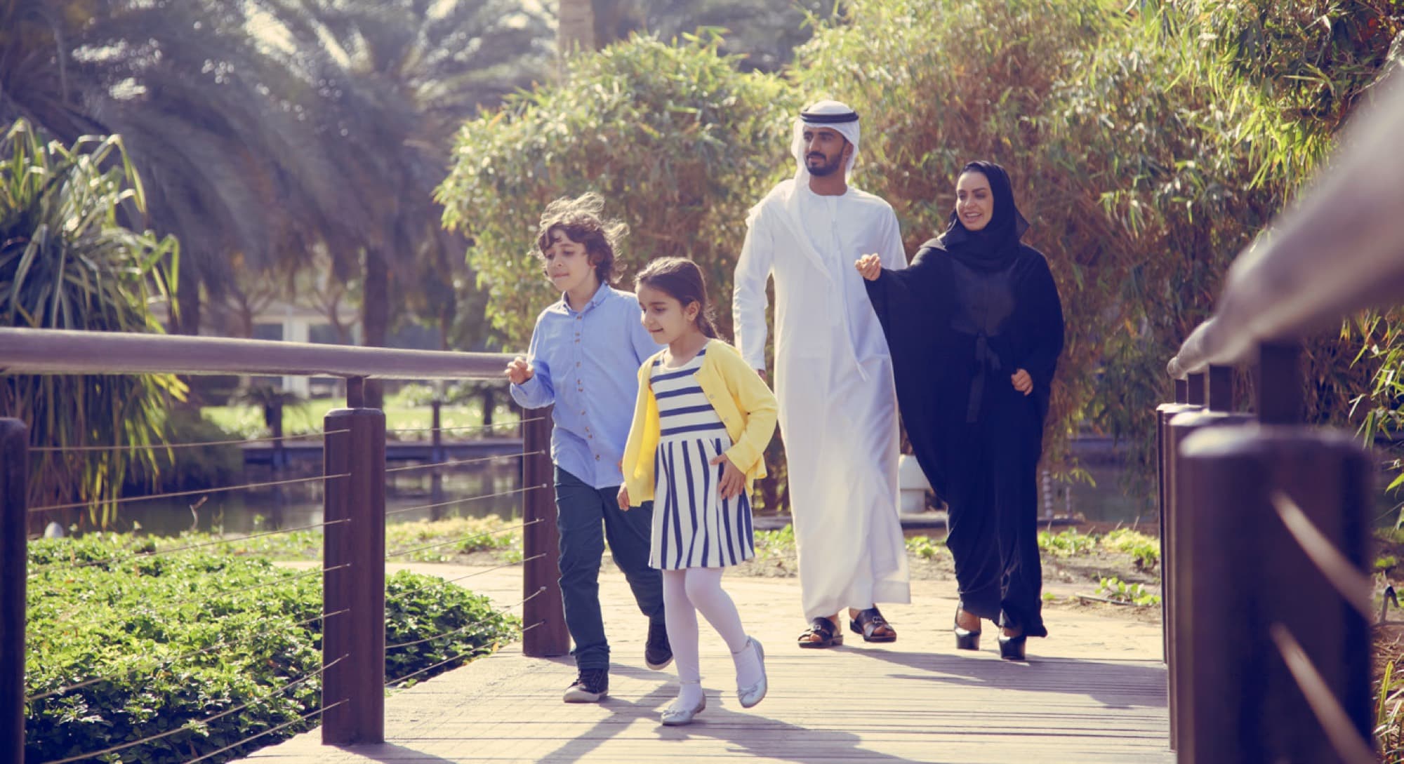 Family walking along a palm-lined boardwalk in Arabian Ranches 3. AR3 Living is your go-to local expert on community service charges.