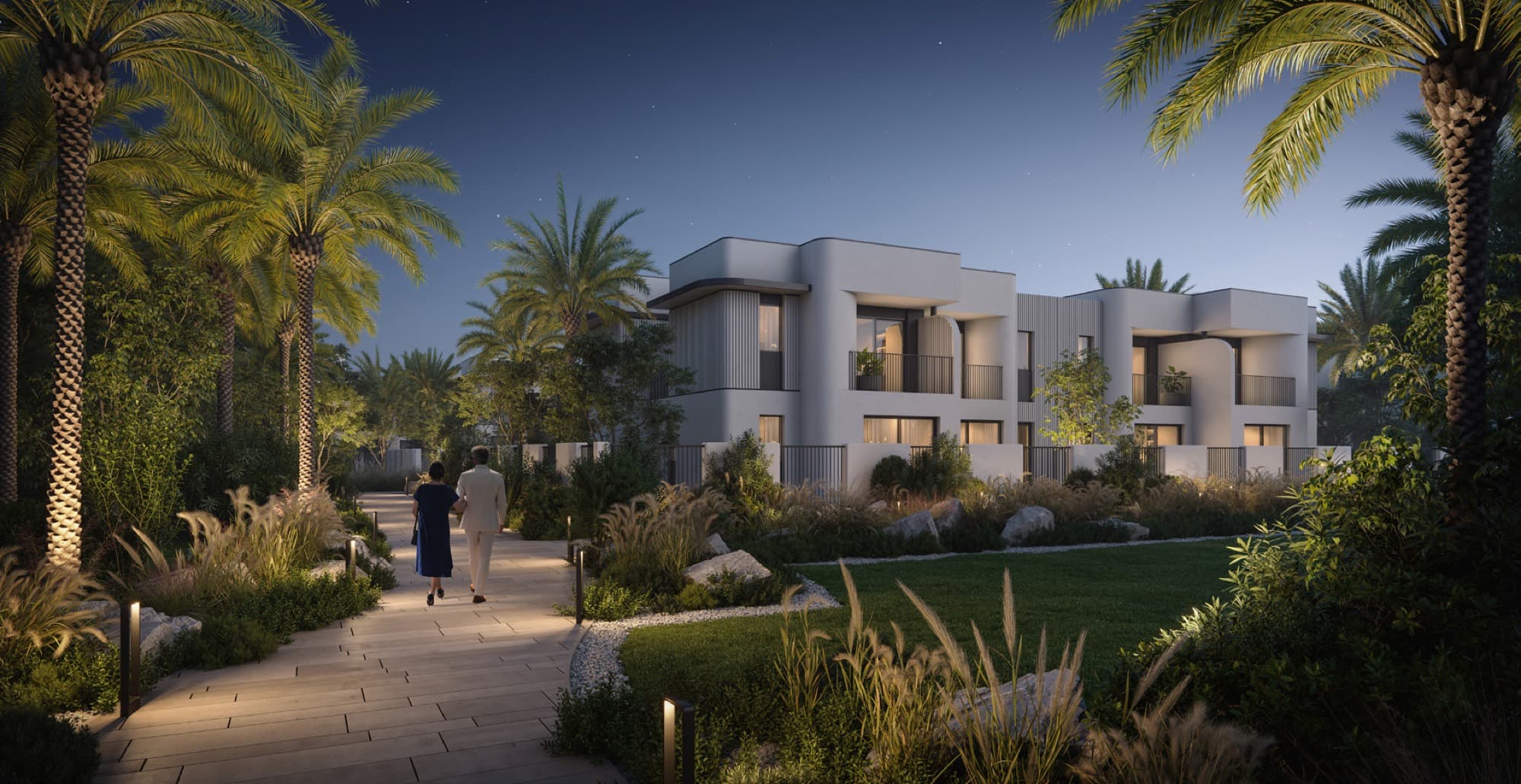Dusk view of Anya townhouses, Arabian Ranches 3, showing a curved white façade and lit interiors along a palm-lined path.