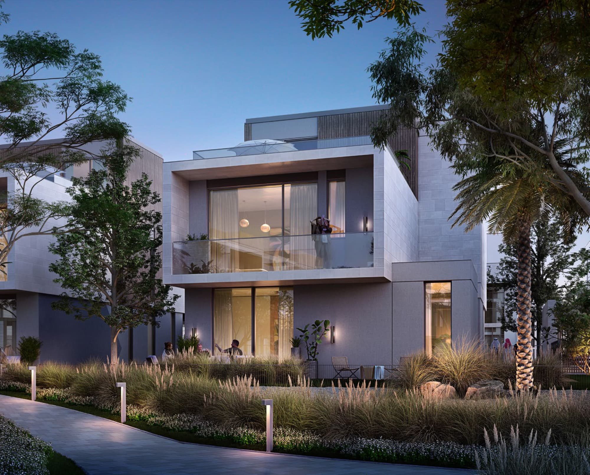 Dusk exterior of an Elie Saab villa in Arabian Ranches 3, stone façade with glass balcony and mature landscaped garden.
