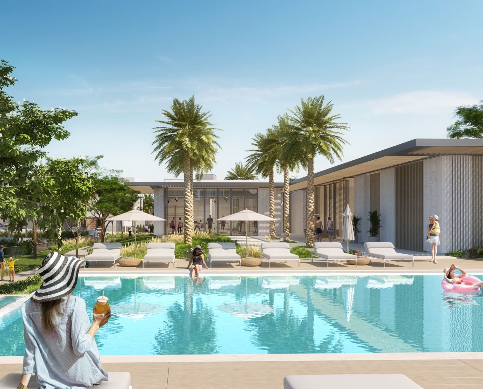 Resort-style pool at Elie Saab Villas, Arabian Ranches 3, with sun loungers, palm trees and the clubhouse building behind.
