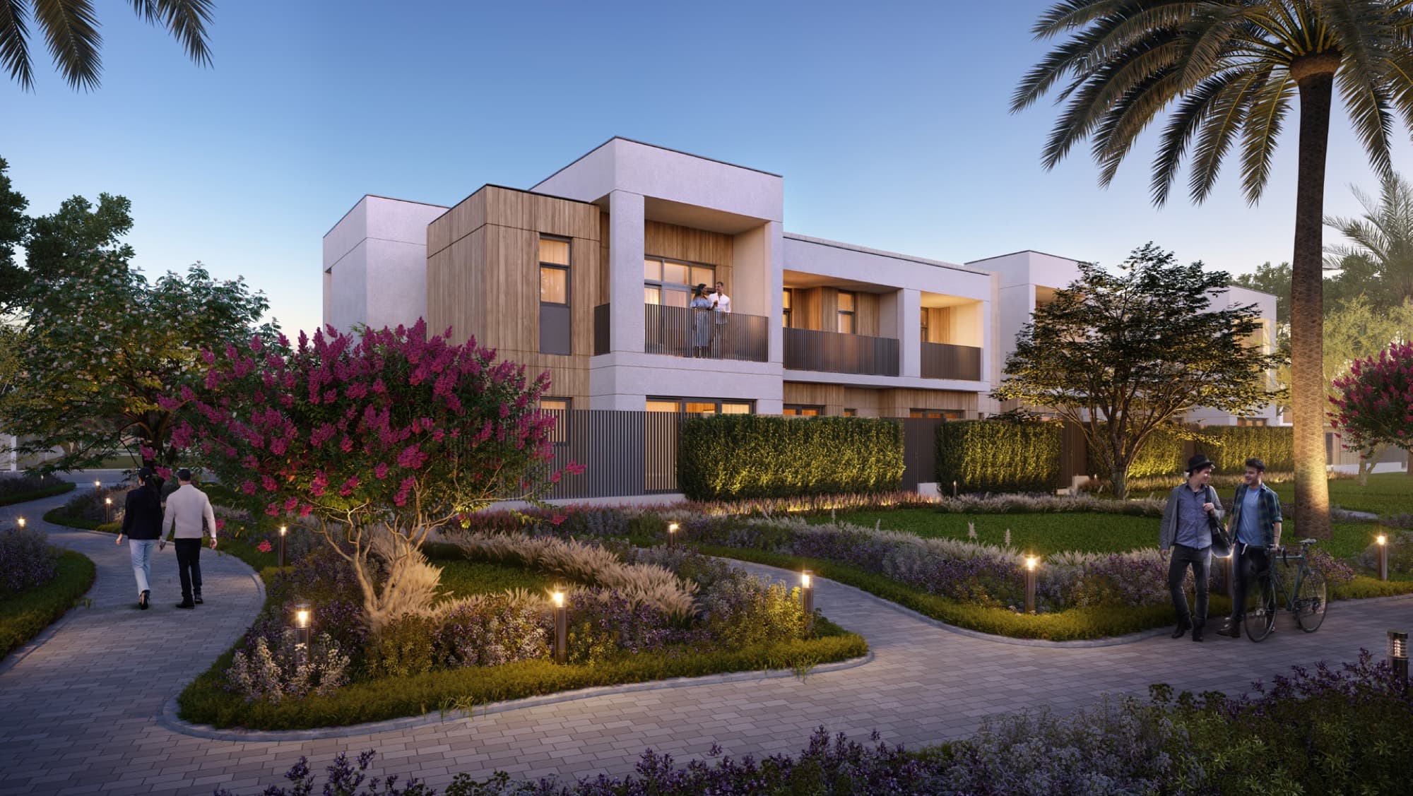 Dusk exterior of a Raya townhouse in Arabian Ranches 3, Dubai, with a couple on the balcony above a flowering tree.