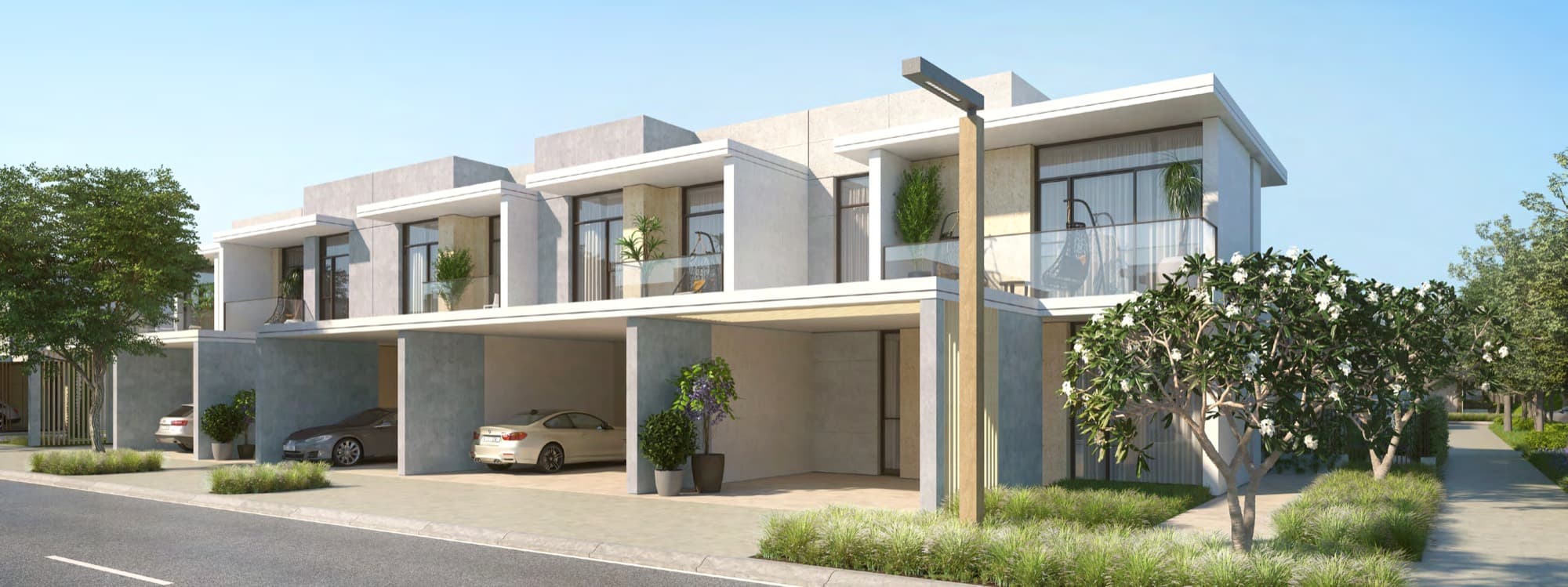 Street view of Ruba townhouses with carports, balconies and flowering shrubs, Arabian Ranches 3, Dubai.